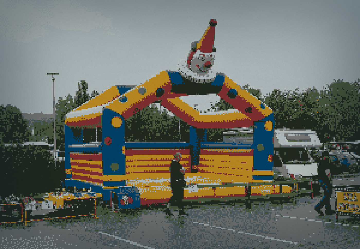 Empty inflatable clown-faced bouncy castle on wet asphalt during a rainy market day with no children present.